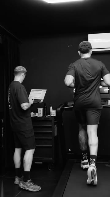 Member training on a treadmill in the altitude room while coach records data on a laptop